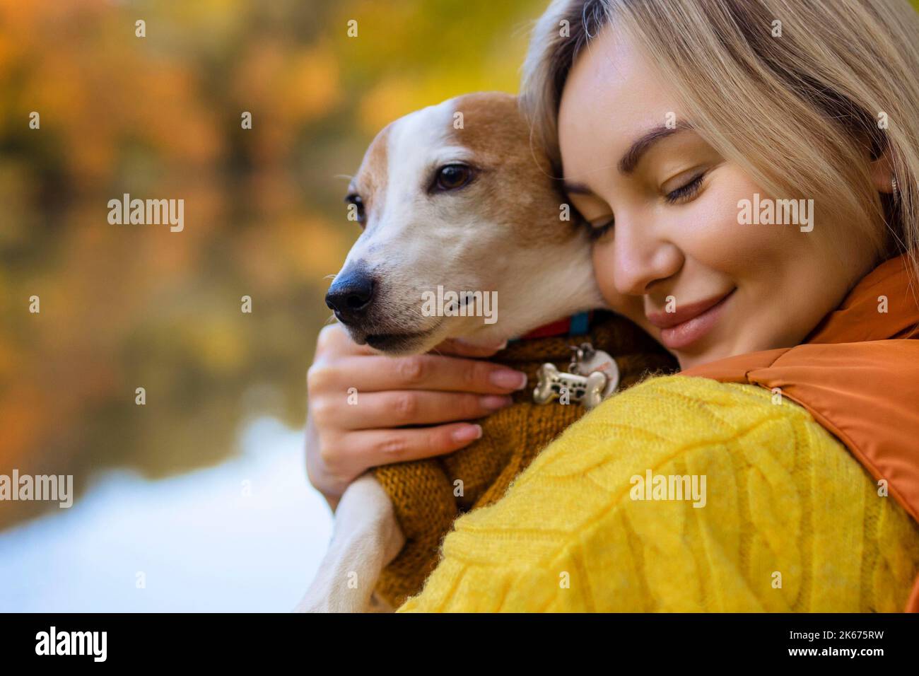 Ritratto di una giovane donna sorridente che bacia un cane in un campo. Ragazza elegante amante del cane che abbraccia il suo cane mentre cammina. Concetto di amicizia animale Foto Stock