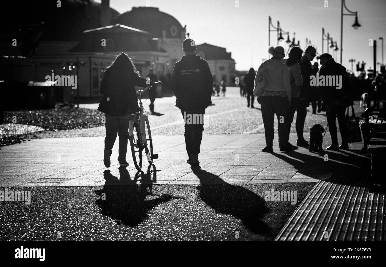 Le persone camminano sotto il sole del tardo pomeriggio sul lungomare di Worthing, West Sussex, Regno Unito. Foto Stock