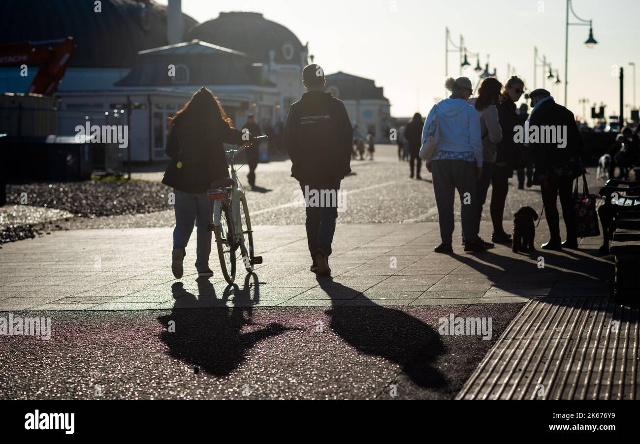 Le persone camminano sotto il sole del tardo pomeriggio sul lungomare di Worthing, West Sussex, Regno Unito. Foto Stock
