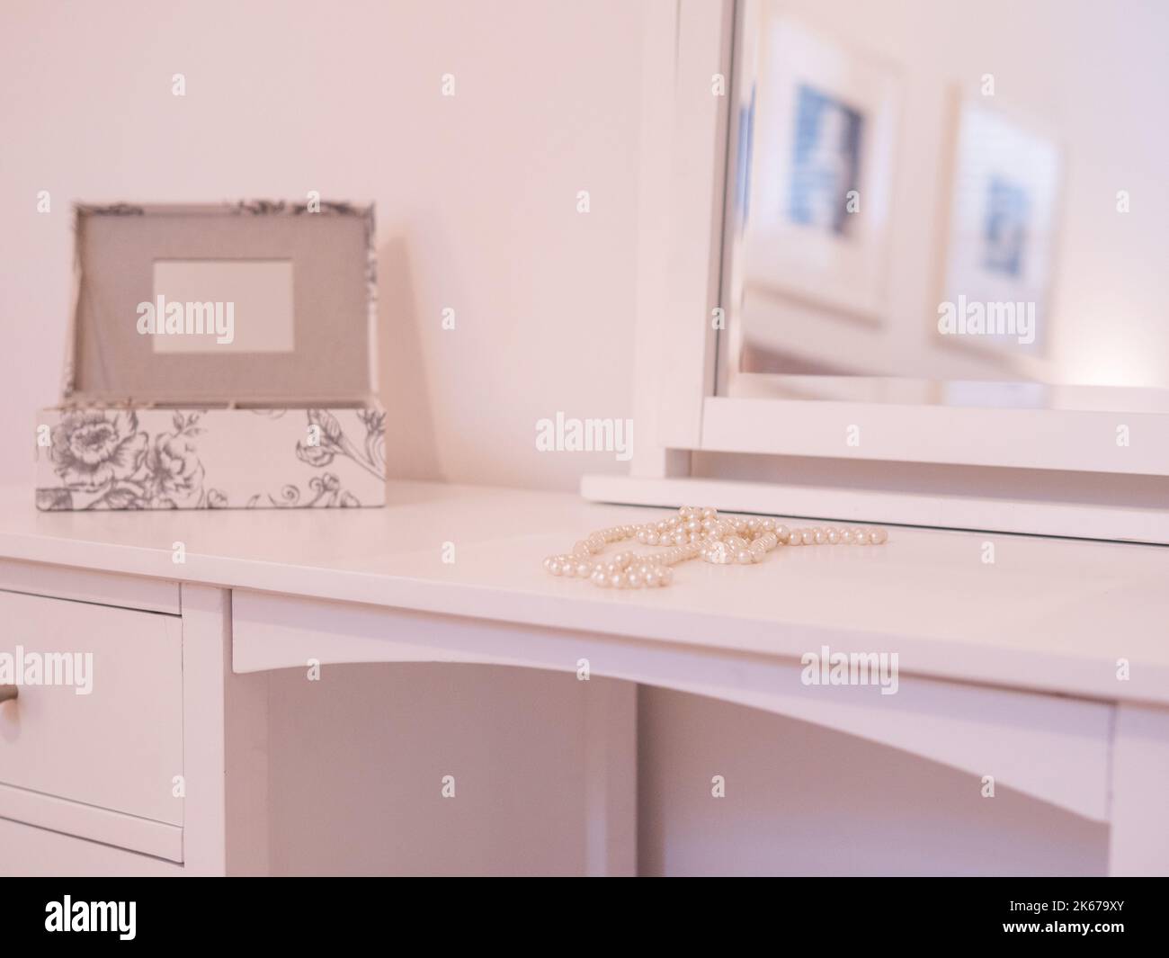 Una foto selettiva di una collana di perle e di una scatola di gioielli su un tavolo vestito bianco con uno specchio Foto Stock