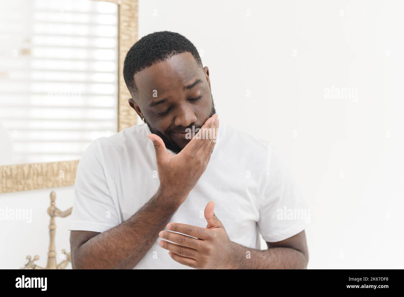 Ritratto di giovane afroamericano che applica crema nutriente del viso o balsamo in vasca da bagno, concetto di cura della pelle. Foto Stock