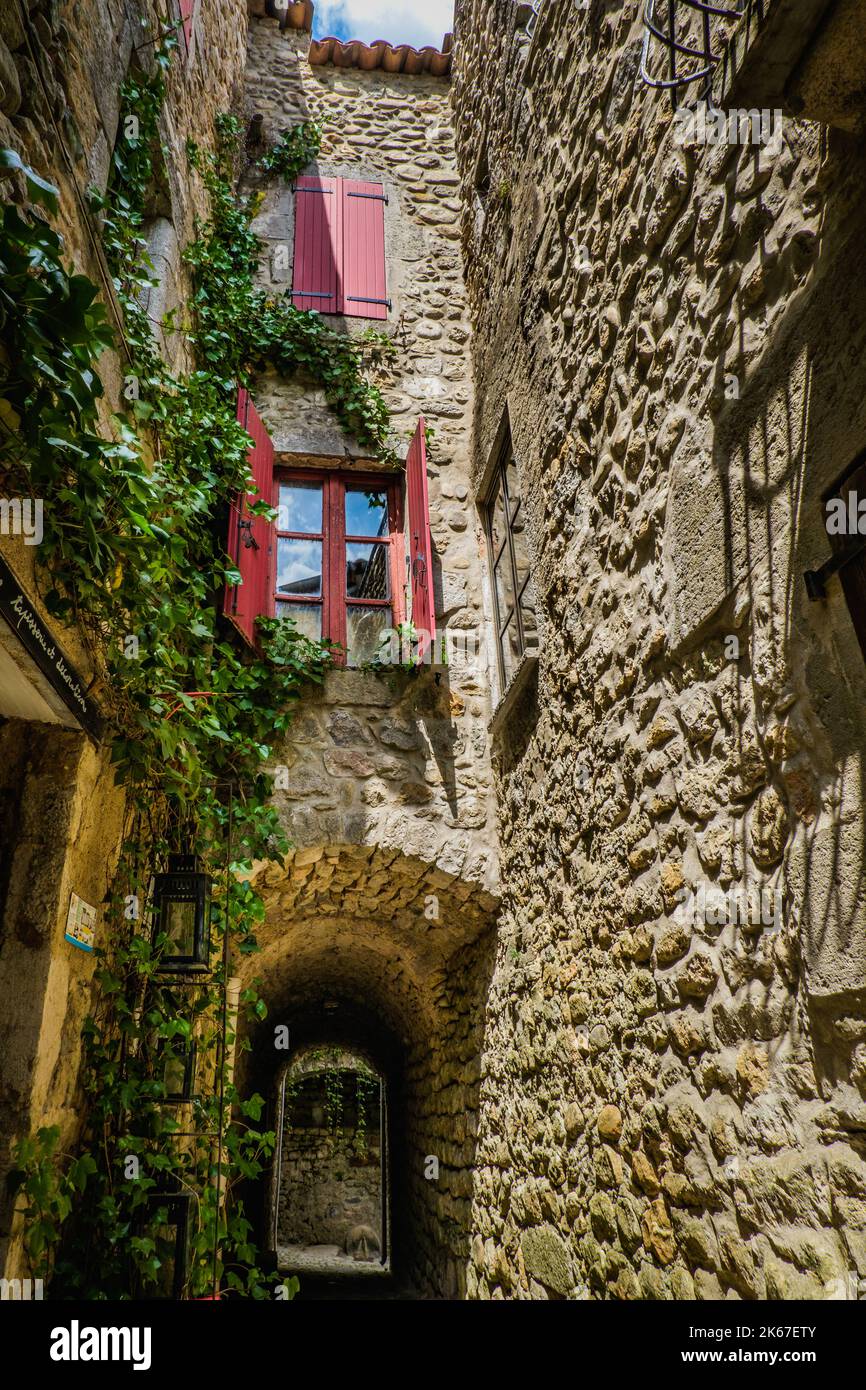 Persiane rosse, la vite e la facciata in pietra di una casa medievale nel villaggio di Labeaume nel sud della Francia (Ardeche) Foto Stock