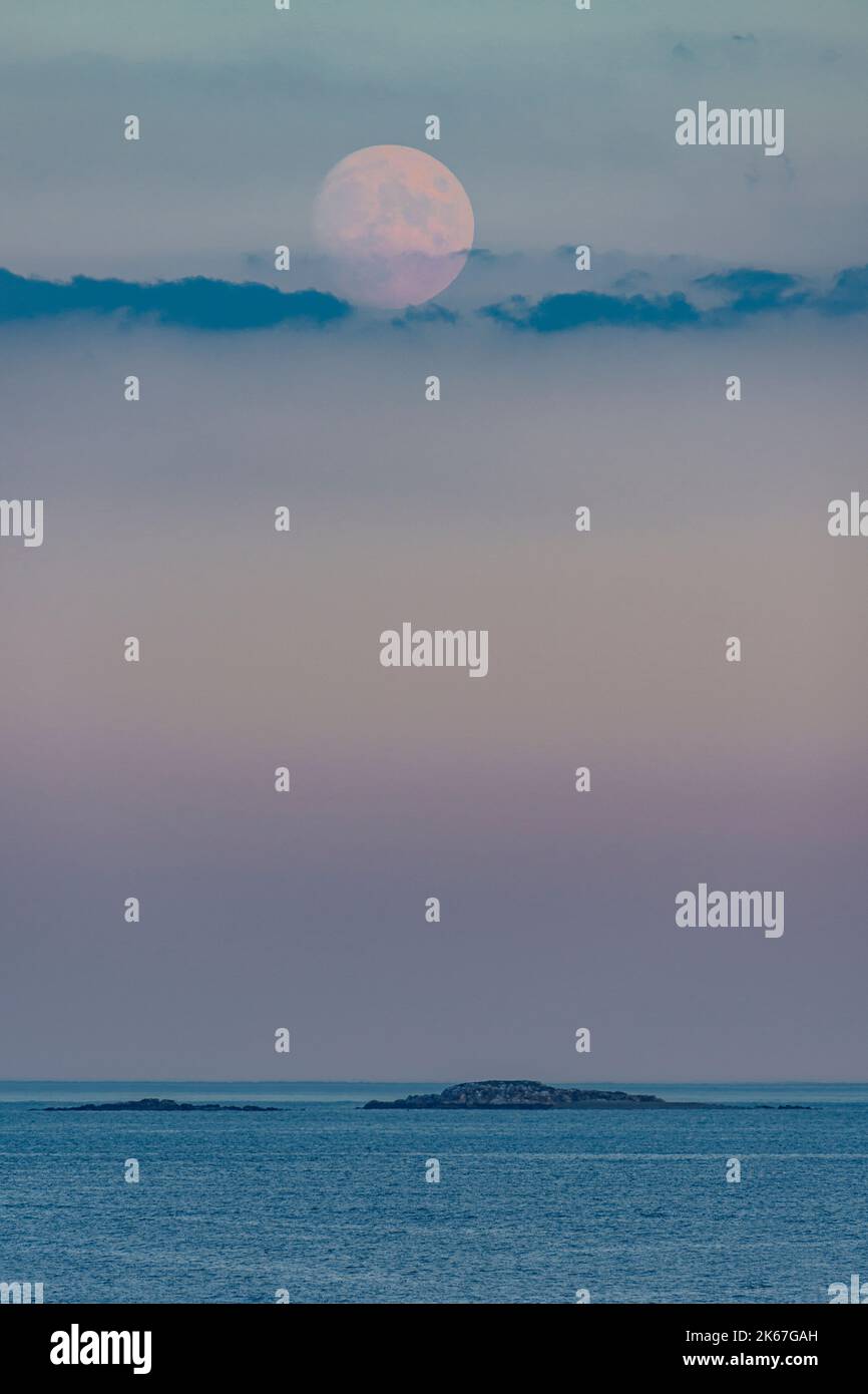 Il 96% dei Cacciatori illuminati Luna Peeking attraverso le nuvole sopra il canale e due piccole isole Foto Stock