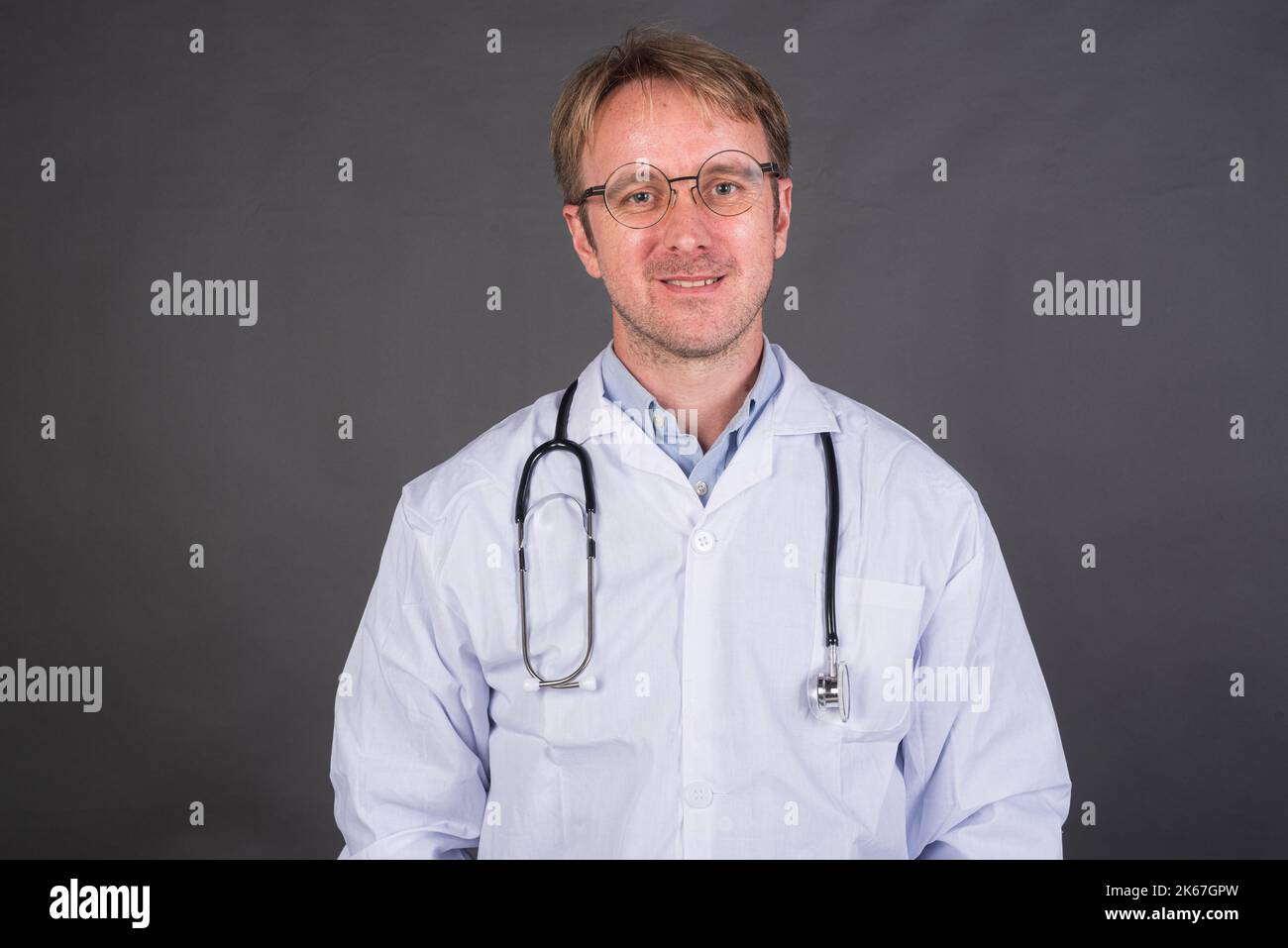 Felice medico maschile con stetoscopio sul collo in mantello medico contro sfondo grigio Foto Stock