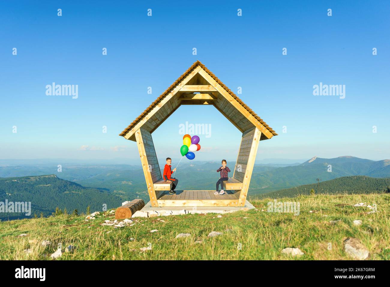 Una ragazza e un ragazzo sono seduti in una casa di legno su una montagna che regge palloncini. Concetto di sicurezza, assicurazione e futuro luminoso Foto Stock