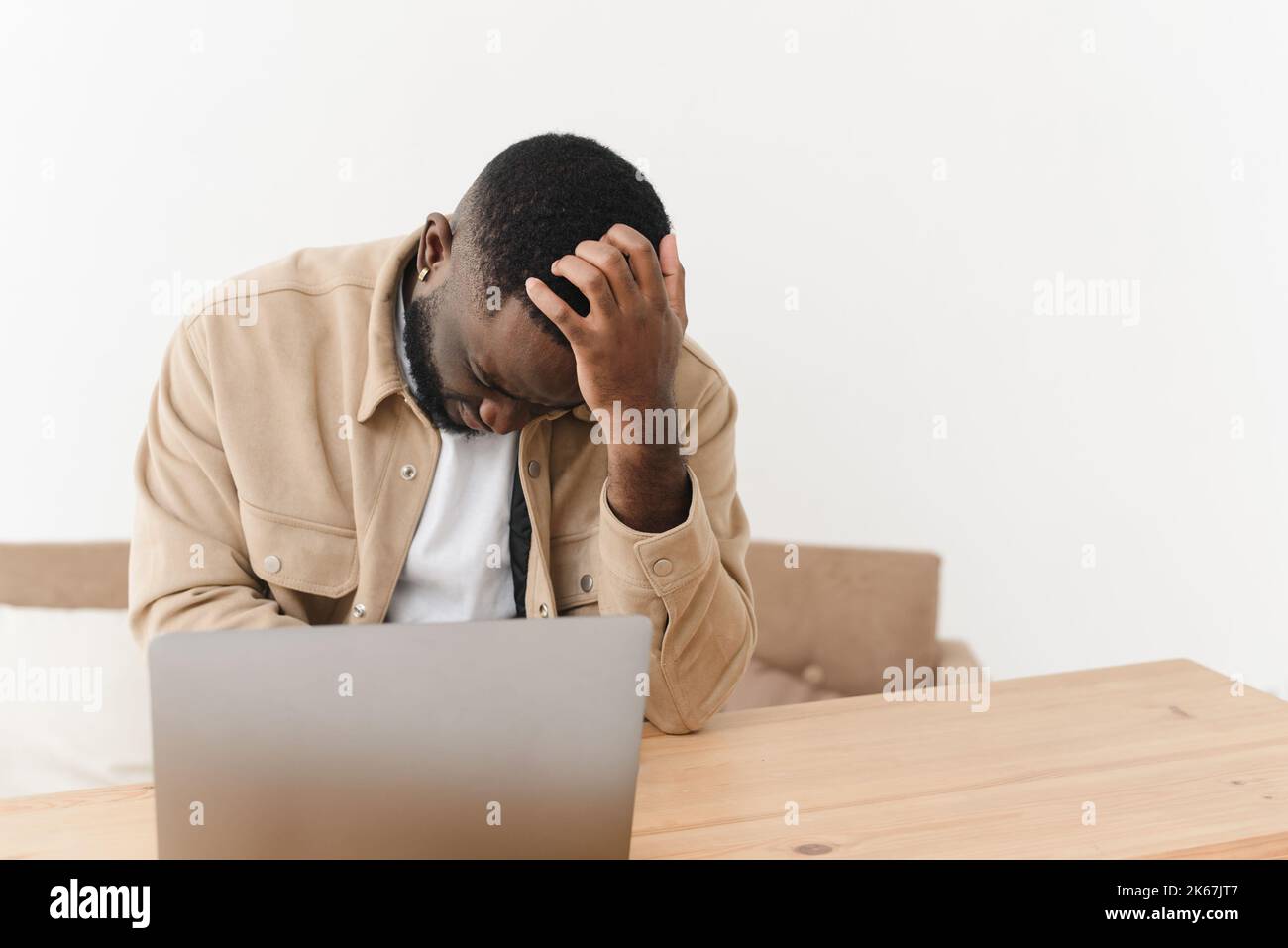 Il giovane uomo nero ha lavorato in modo eccessivo, soffrendo di mal di testa mentre si siede al portatile a casa Foto Stock