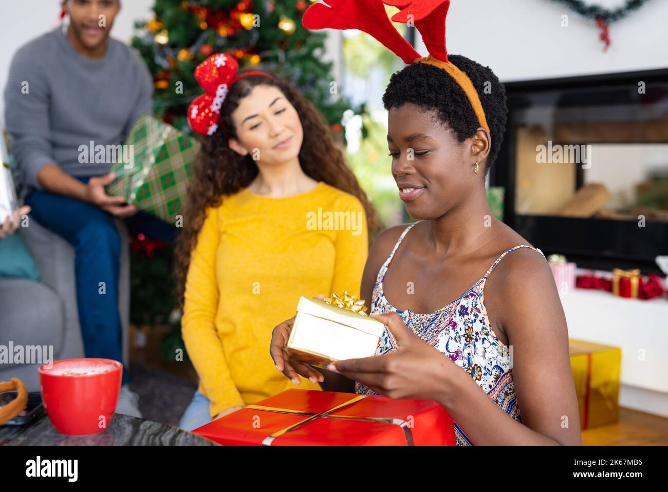Immagine di felici e diversi amici femminili che celebrano il natale a casa scambiando regali Foto Stock