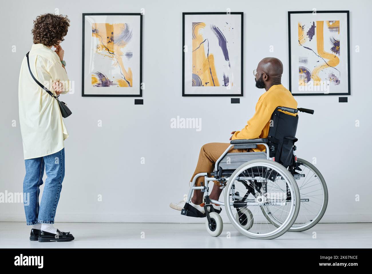 Vista posteriore di una giovane donna e di un uomo con disabilità che guarda le foto alla galleria d'arte Foto Stock