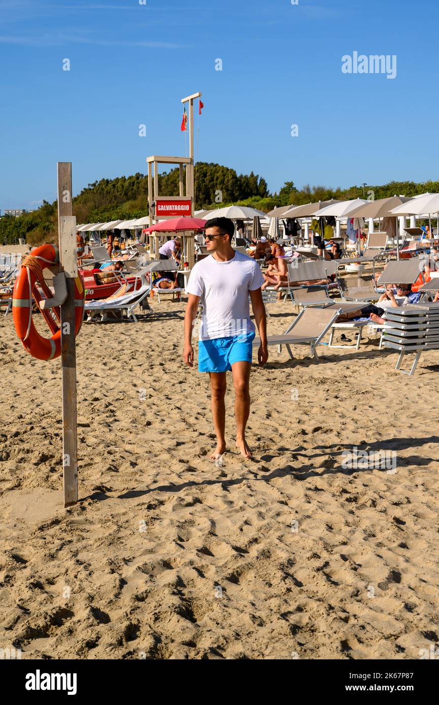 Un giovane di gara mista nei suoi venti cammina verso la telecamera sulla spiaggia di Sottovento a sud di Gallipoli in Puglia. Foto Stock
