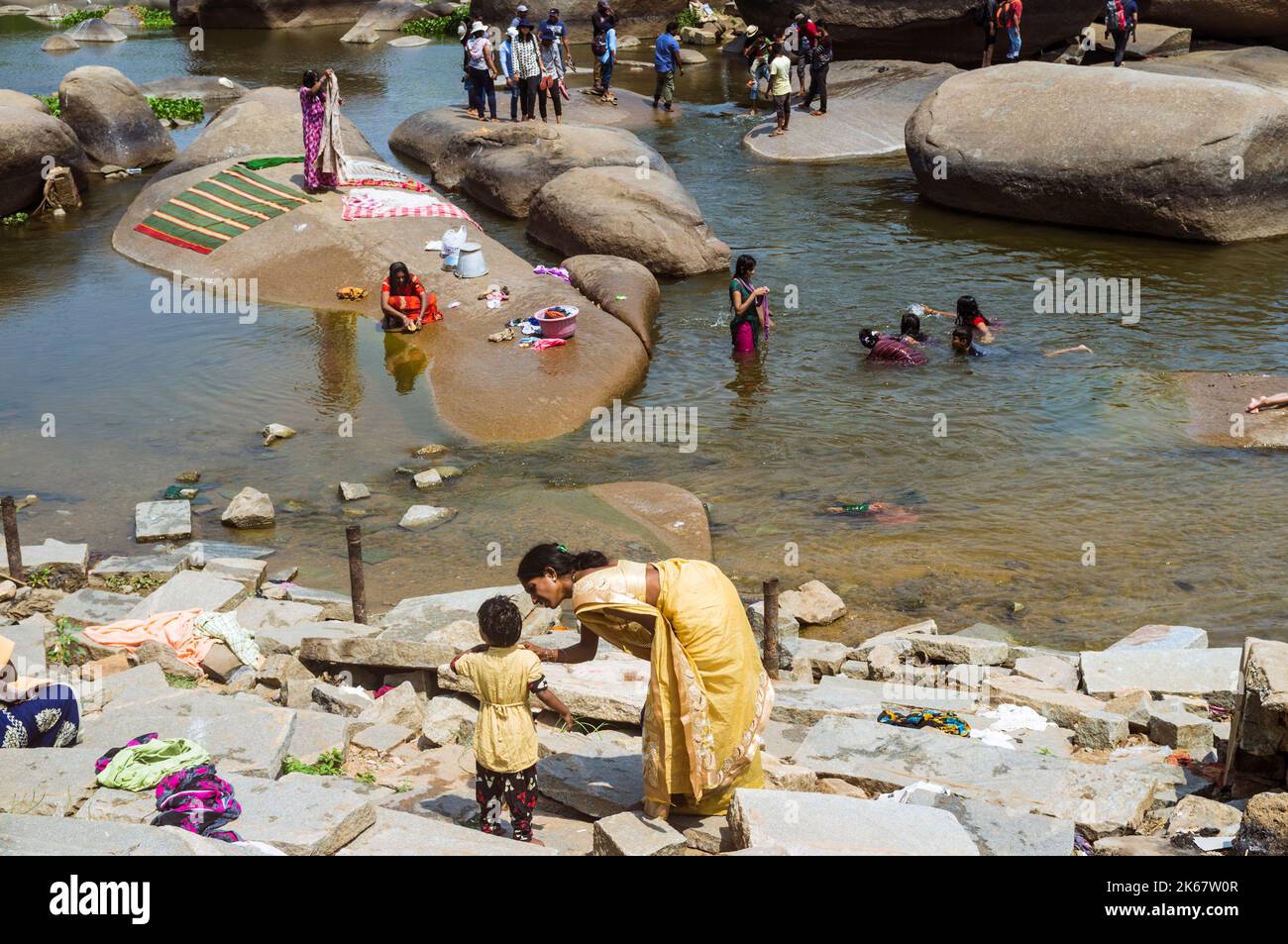 Hampi, Karnataka, India: Una madre e suo figlio guardano un gruppo di donne che si lavano sui massi del fiume Tungabadra. Foto Stock