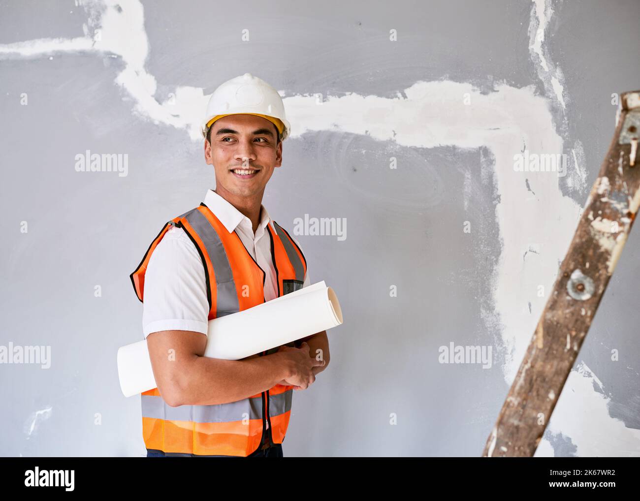 Un attraente operaio asiatico di costruzione tiene i programmi della costruzione sotto il suo braccio Foto Stock