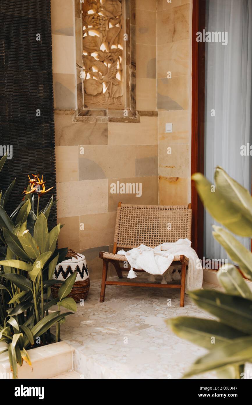 Sedia in vimini con coperta bianca sulla veranda estiva. Arredamento casalingo in stile balinese. Verticale Foto Stock