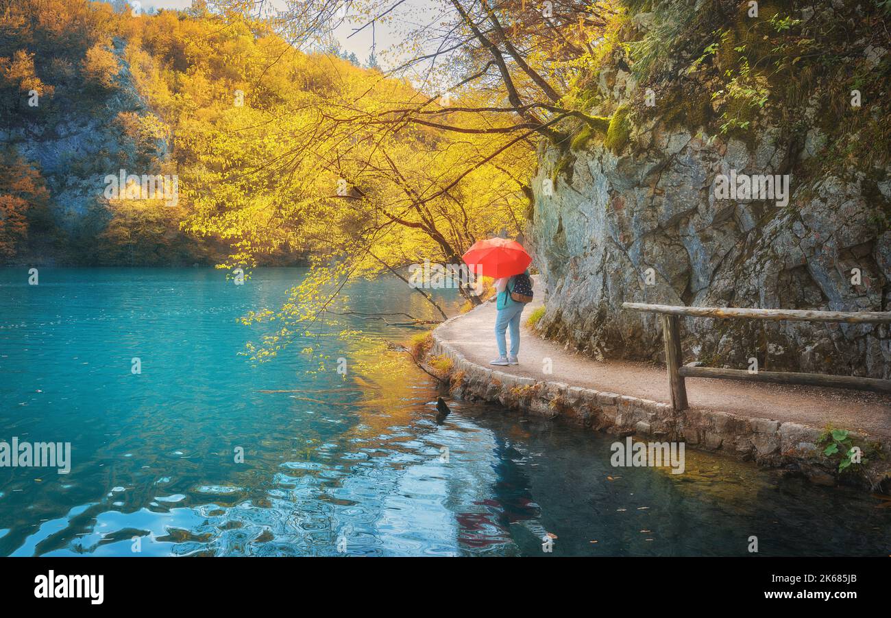 Donna con ombrello rosso sul sentiero sotto gli alberi gialli vicino al lago Foto Stock