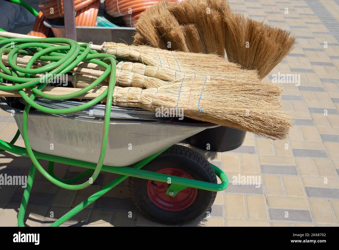 Scopa e tubi flessibili in gomma su una carriola. Vendita per il giardino. Copia spazio per il testo. Foto Stock