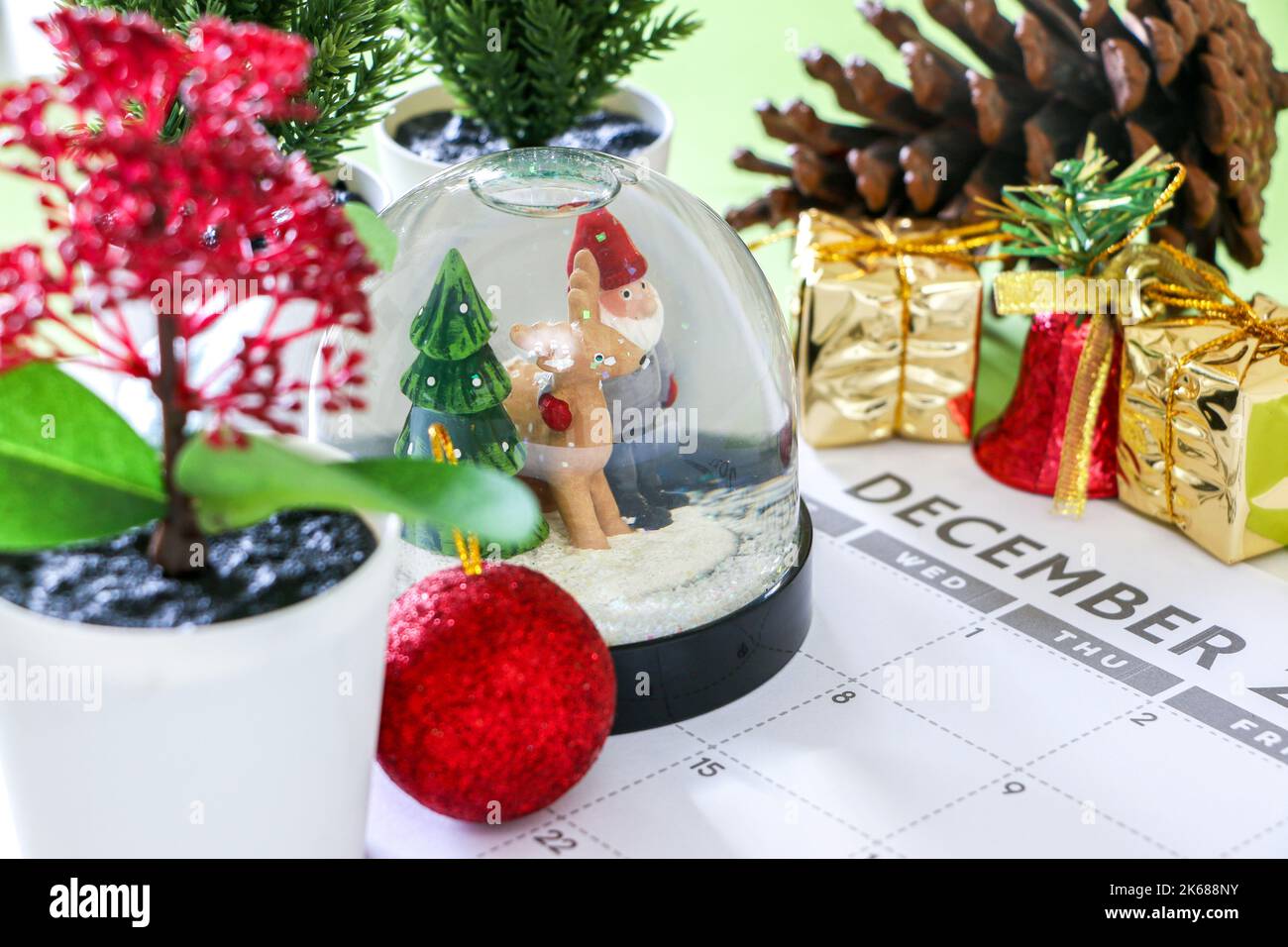 Concetto di Natale colorato, globo di neve festivo e altre decorazioni su calendario di dicembre, pini, pinone, doni, campana e baule, Buon Chris Foto Stock