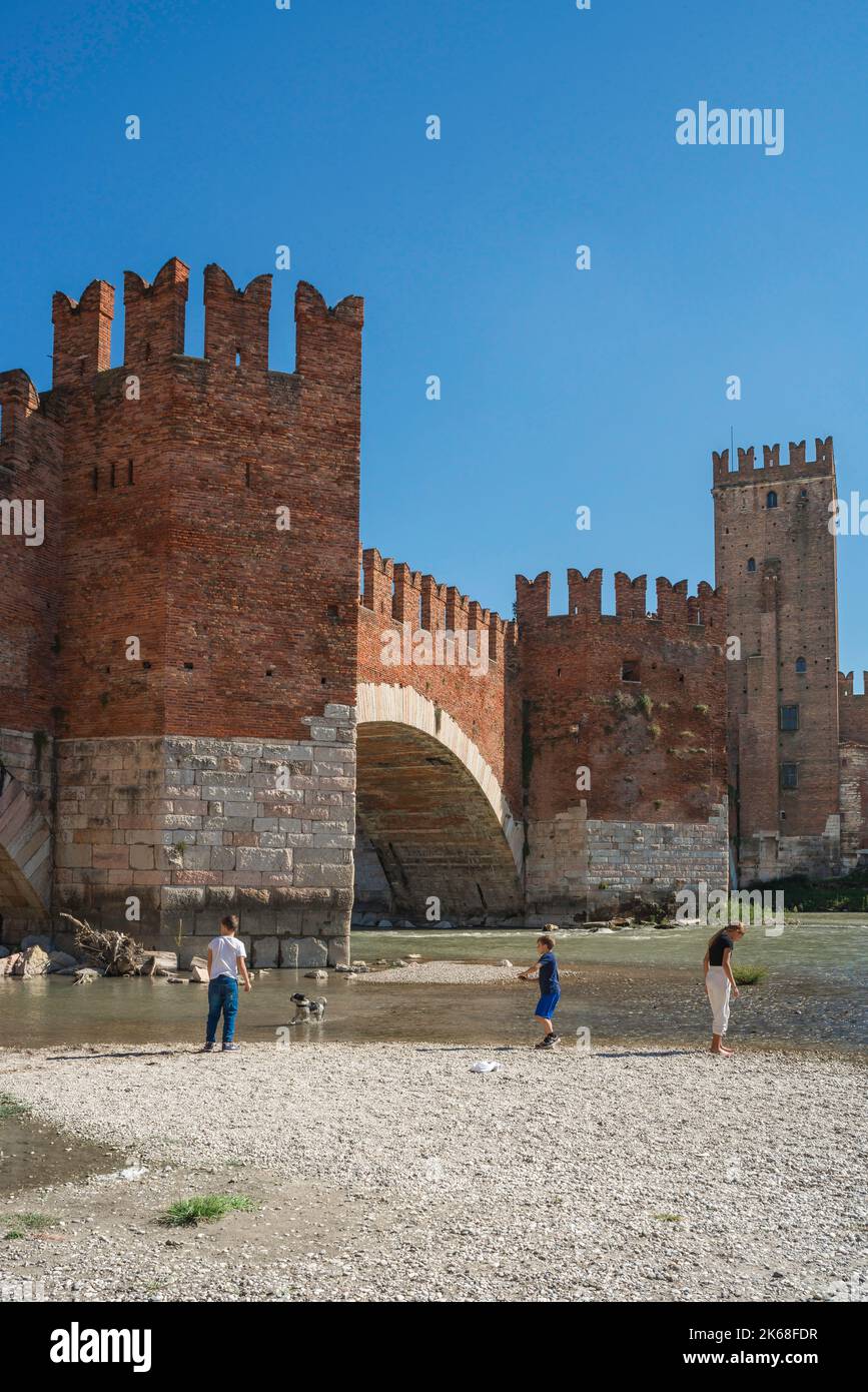 Ponte di Verona, vista in estate del Ponte Scaligero e dei giovani che si trovano lungo il fiume Adige nella storica città di Verona Foto Stock