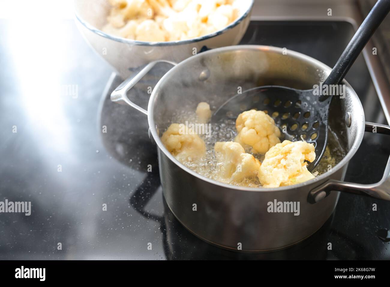 I fiori di cavolfiore vengono fritti in una pentola con olio caldo in stufa, preparazione di un pasto vegetale, spazio copia, fuoco selezionato, profondità stretta Foto Stock