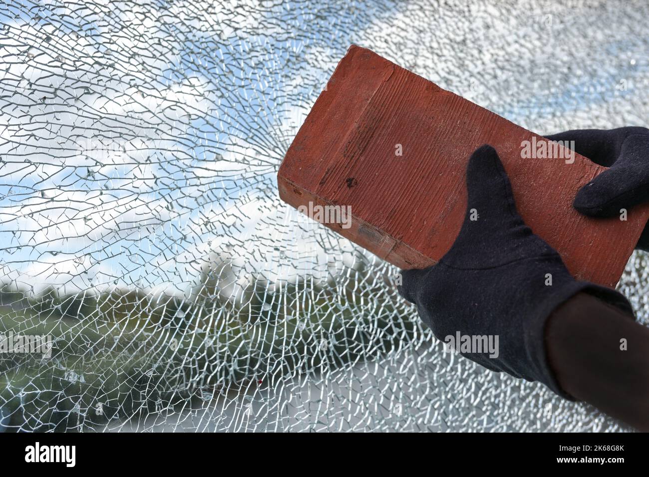 Le mani con un mattone stanno distruggendo una finestra di vetro di sicurezza laminata, il concetto di violenza e vandalismo, lo spazio di copia, il fuoco selezionato Foto Stock