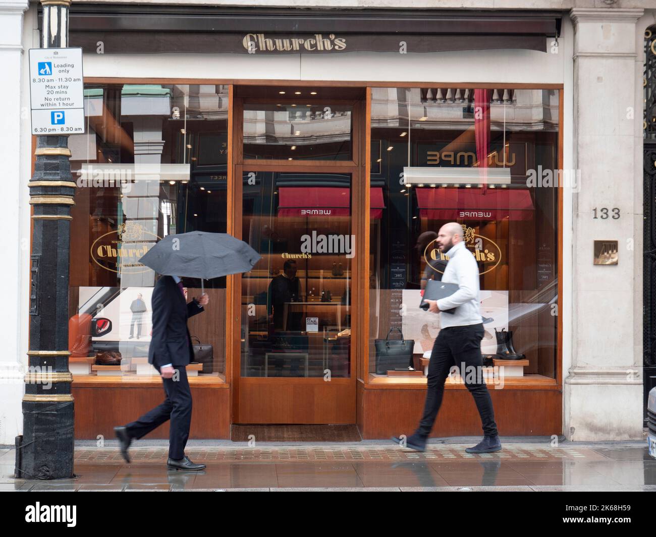 Mayfair, Londra, Regno Unito, il negozio di scarpe di lusso della Chiesa, con gli acquirenti che camminano accanto con gli ombrelli sotto la pioggia Foto Stock