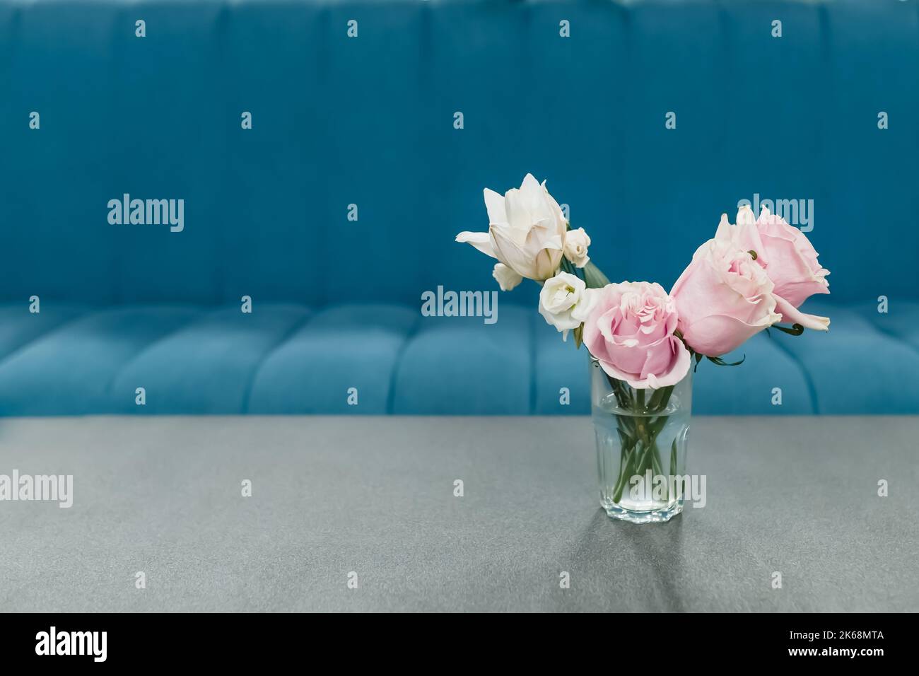 Fiori rosa in vaso su tavolo grigio con divano blu sullo sfondo. Foto Stock