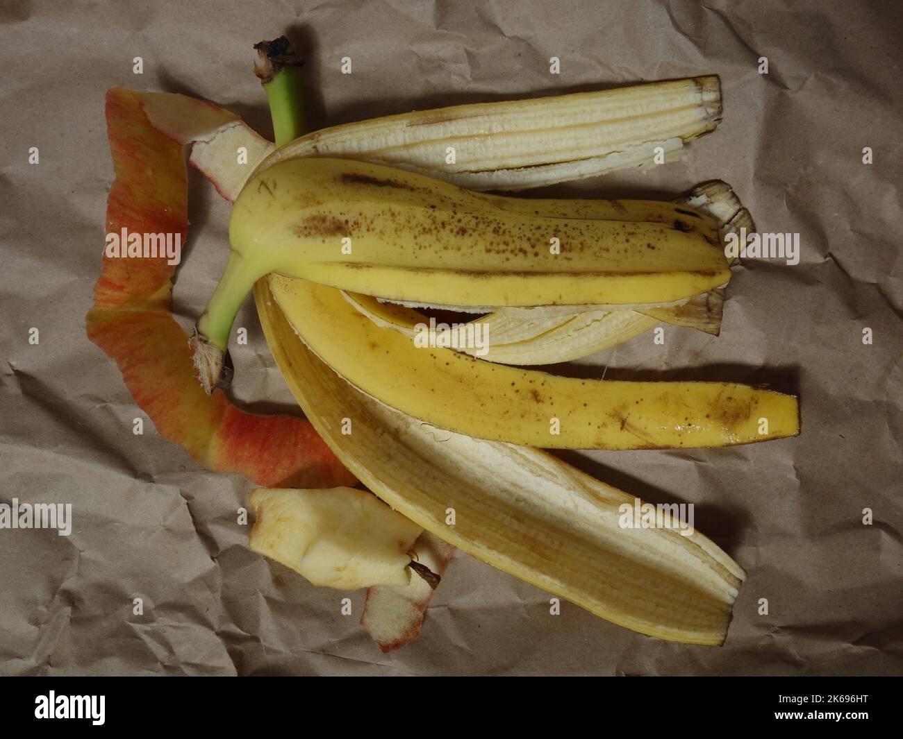 Banane e bucce di mela, rifiuti biodegradabili su carta da imballaggio stropicciata Foto Stock