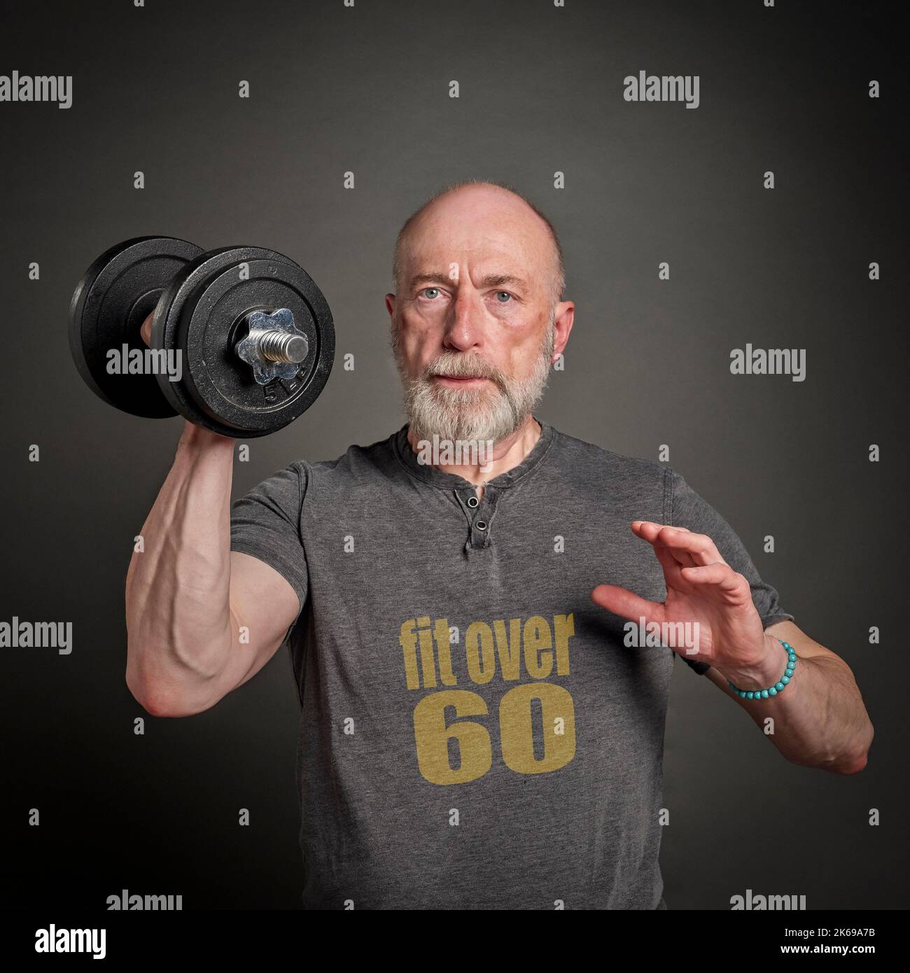 l'uomo calvo e bearded che indossa la maglietta con oltre 60 testo sta esercitandosi con un dumbbell pesante, anziano attivo e concetto di idoneità Foto Stock