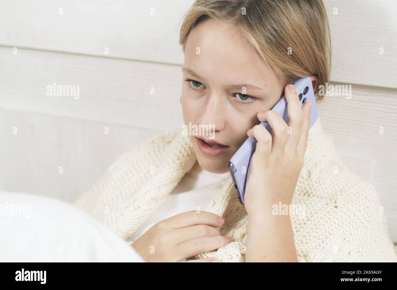 Ragazza teen si siede sul letto e parla emotivamente sul telefono. Foto Stock