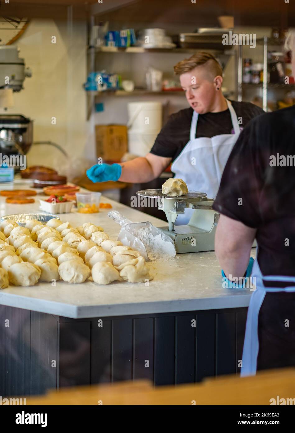Vista attraverso la finestra di una donna che lavora in una panetteria artigianale. Guardando attraverso una finestra da forno dall'esterno. Di fronte al negozio. Editoriale, foto di strada Foto Stock