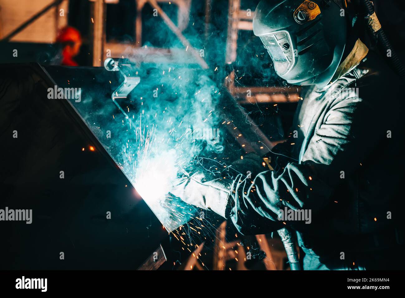 Saldatrice industriale in acciaio in lavorazione in fabbrica di metallo. Scintille e fumo volano dalla saldatura. Foto Stock