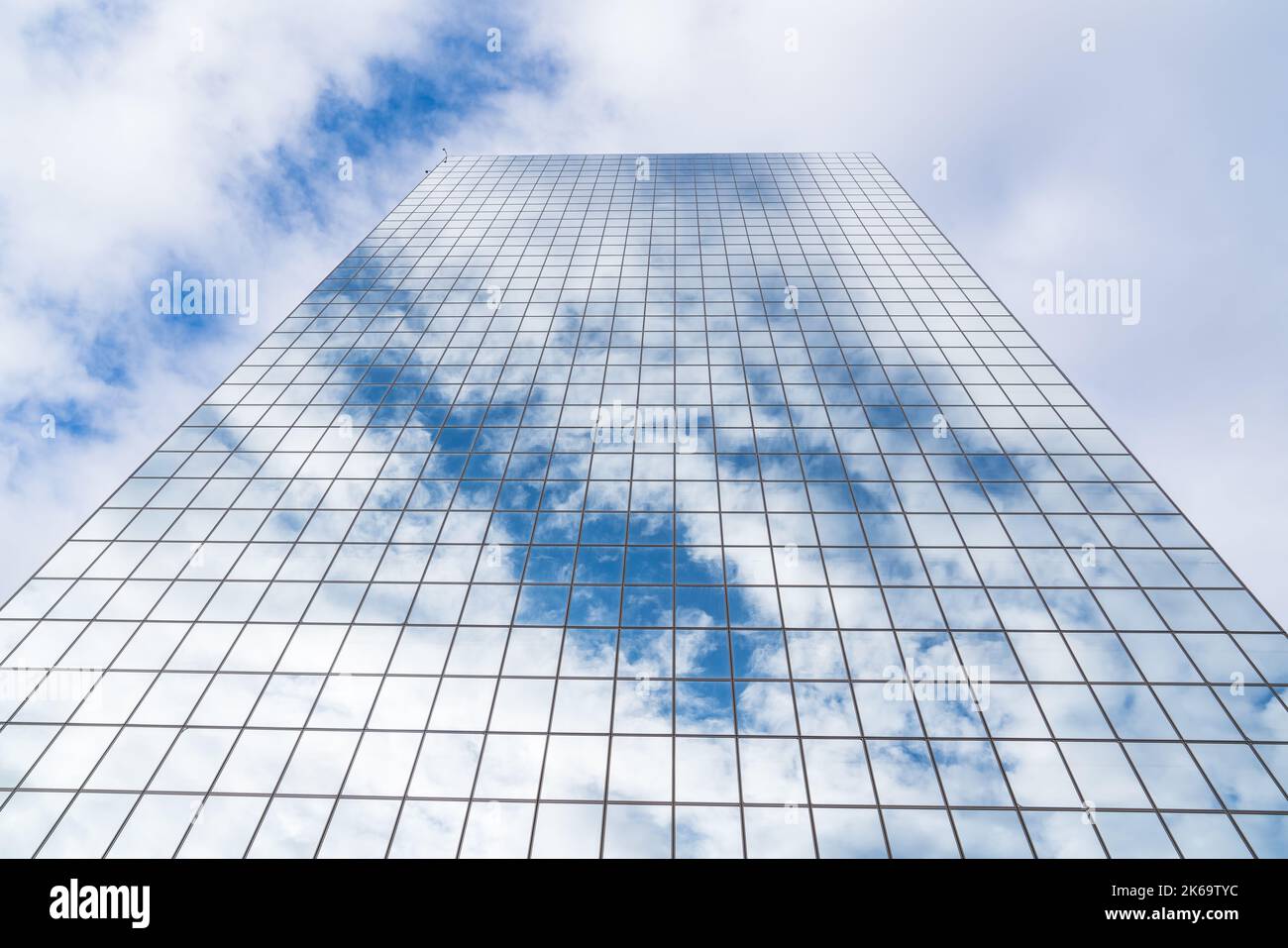 Le nuvole e il cielo blu si riflettono su un alto grattacielo in vetro a specchio Foto Stock