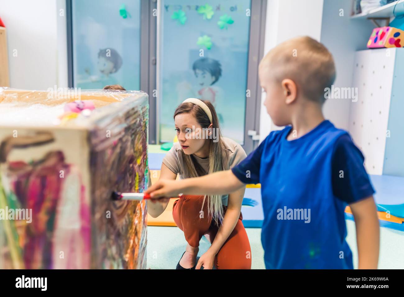 Pittura caucasica preschooler con il suo insegnante sul cellophane in asilo, attività creative per i bambini. Foto di alta qualità Foto Stock