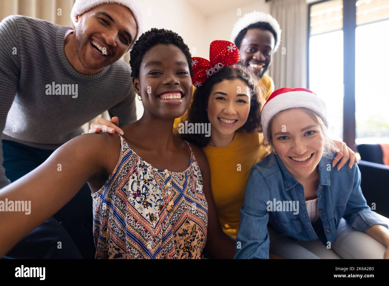 Immagine di amici felici e diversi che celebrano il natale a casa facendo videochiamata di gruppo Foto Stock
