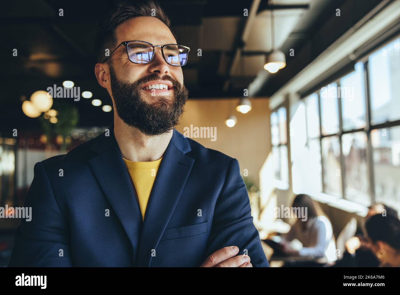 uomo d'affari che pensa a nuove idee di business in uno spazio di co-working. Un uomo d'affari premuroso sorridente mentre sta in piedi con le braccia incrociate. Tu Foto Stock