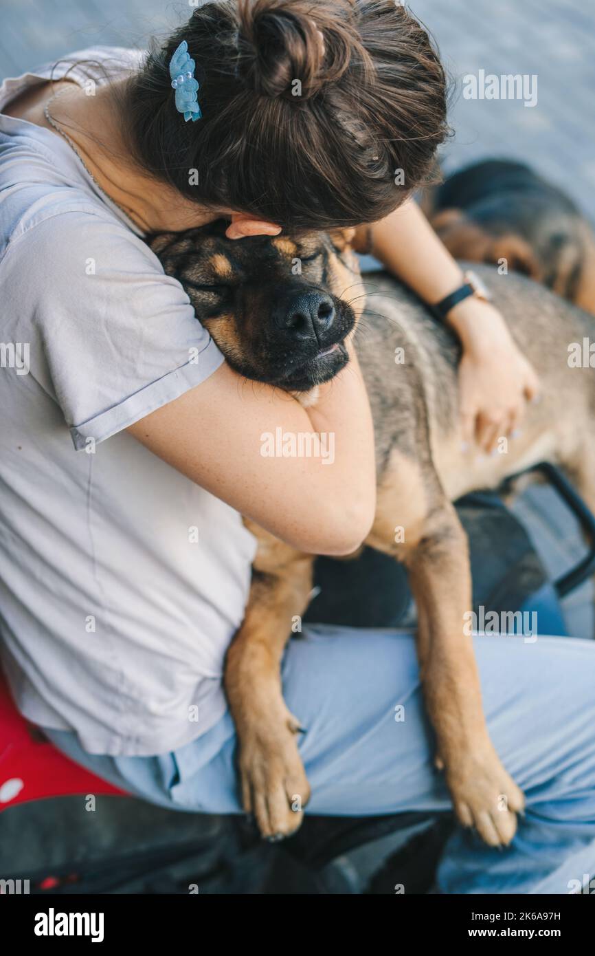 Giovane donna caucasica abbracciare il suo cane da compagnia all'aperto sulla terrazza sul cortile. Concetto di amicizia con gli animali domestici e di trascorrere l'estate felice all'aperto. Foto Stock