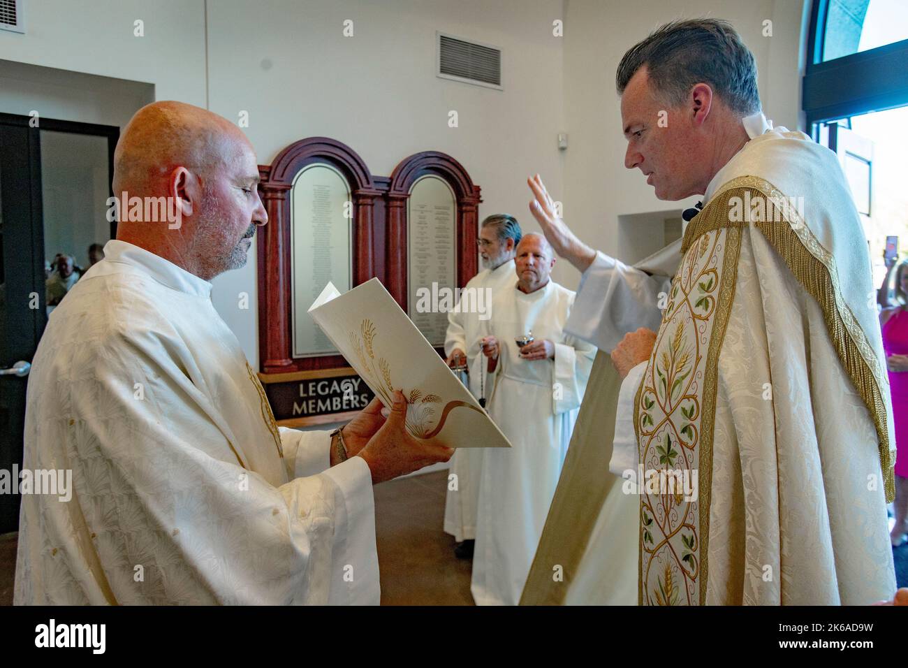 Un diacono contiene un testo mentre il sacerdote di una chiesa cattolica della California meridionale recita un tributo agli ex benefattori della chiesa elencati sulla tavola di bronzo Foto Stock