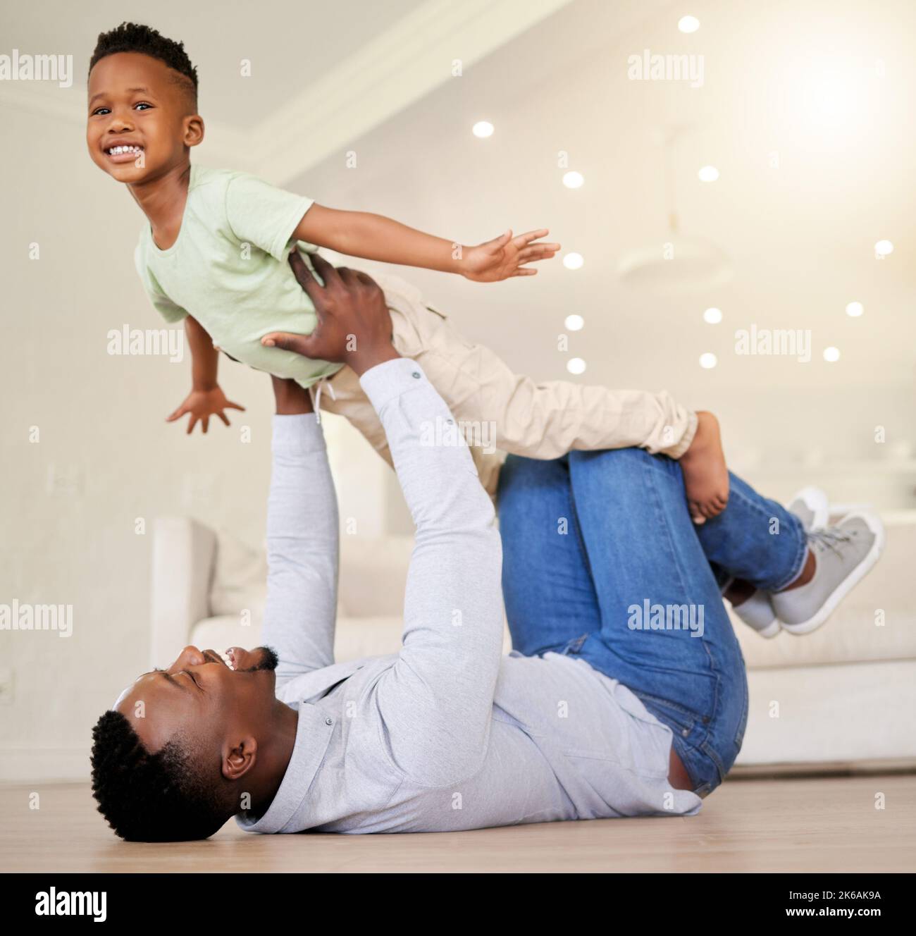 Adorabile ragazzino afroamericano che gioca in salotto fingendo di volare a casa con suo padre. Carino nero bambino maschio sorridente e. Foto Stock