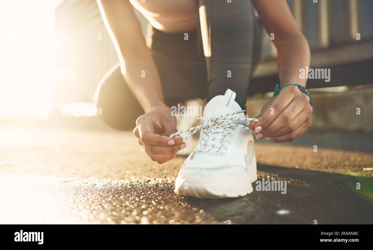 Primo piano di una donna di razza mista legando le scarpe mentre si esercita all'aperto. Scarpe da sneaker bianche con chiusura atleta per una vestibilità comoda e comoda Foto Stock