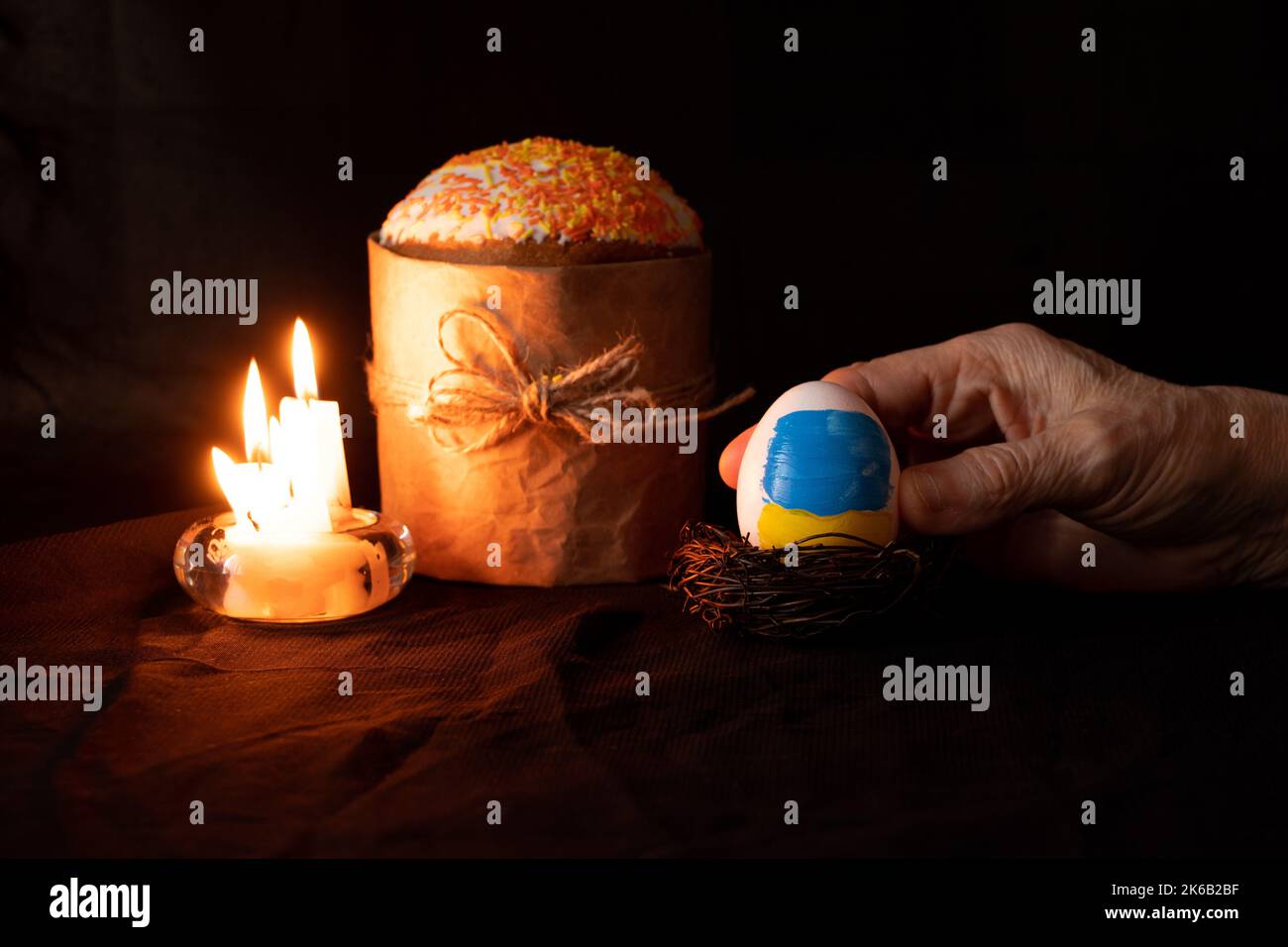 Torta di Pasqua e accanto a un uovo con una bandiera dipinta di Ucraina nelle mani di una donna su uno sfondo nero, candele, vacanze di Pasqua in Ucraina durante Foto Stock