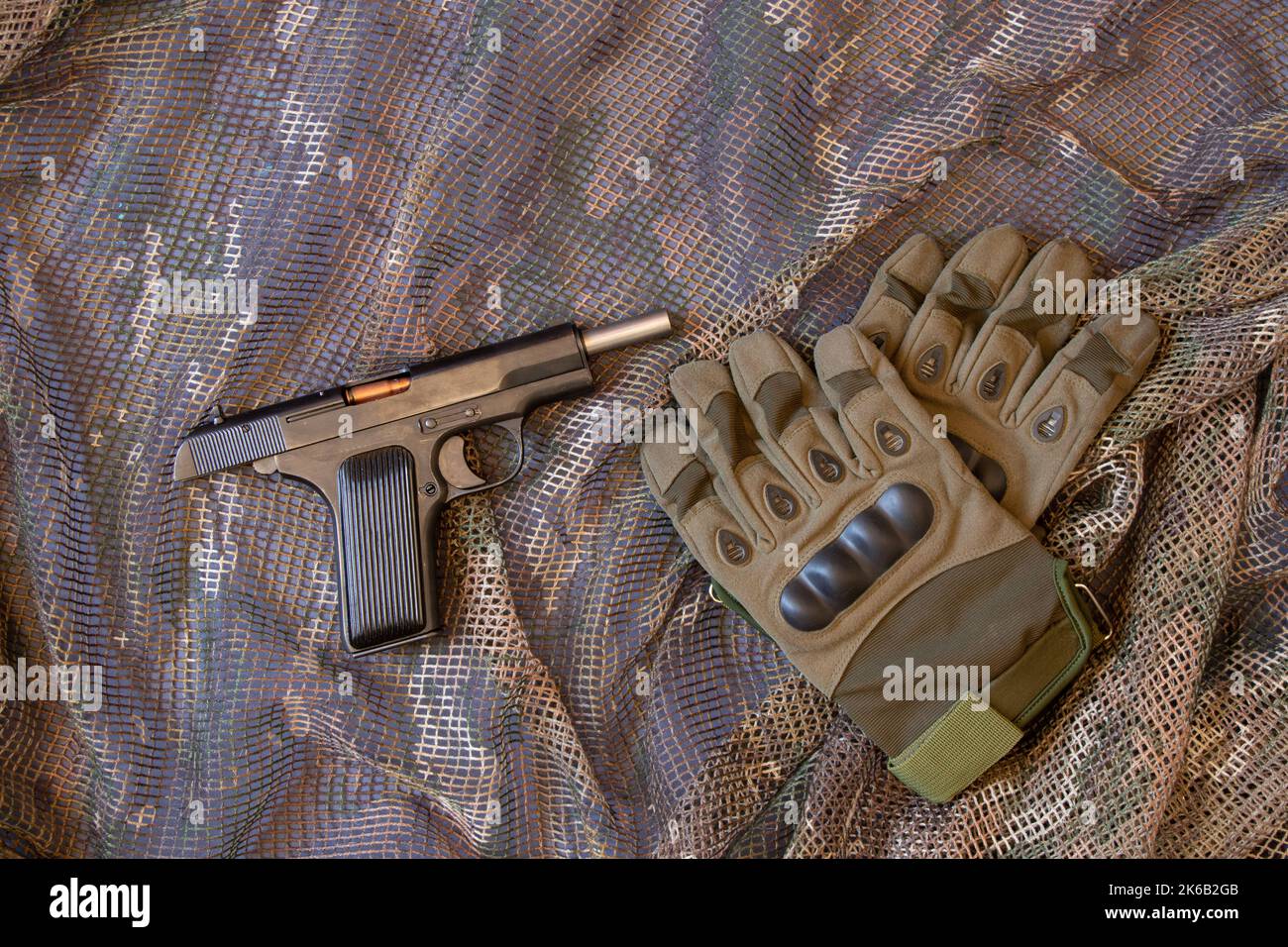 Pistola e guanti militari di un soldato su una griglia mimetizzazione, uniforme militare e armi, guerra Foto Stock
