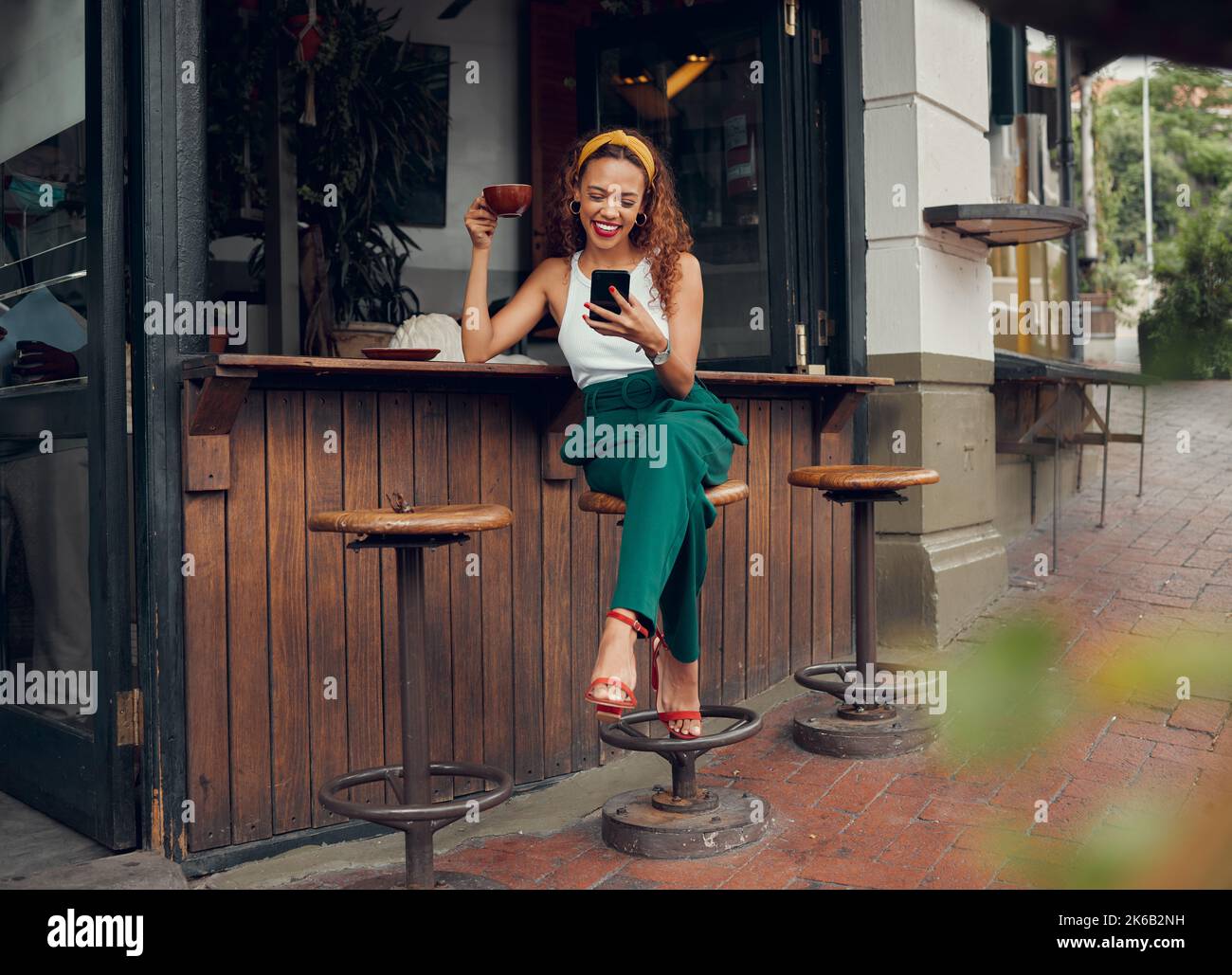 Telefono, social media e caffè con una donna nera al bancone del bar sul marciapiede. Caffetteria, internet e comunicazione con un giovane Foto Stock