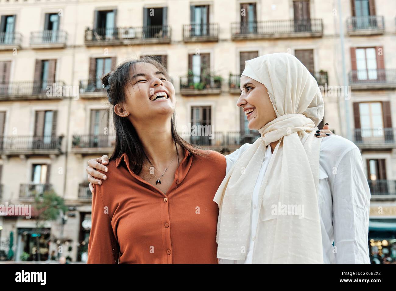 Amici femminili multietnici che si abbracciano e ridono mentre si divertono insieme all'aperto per strada. Foto Stock