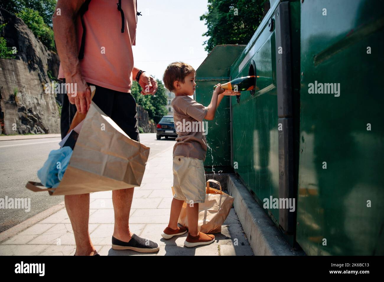 Vista laterale del ragazzo che sta in piedi con il nonno e che ha travollato una bottiglia in un cestino Foto Stock