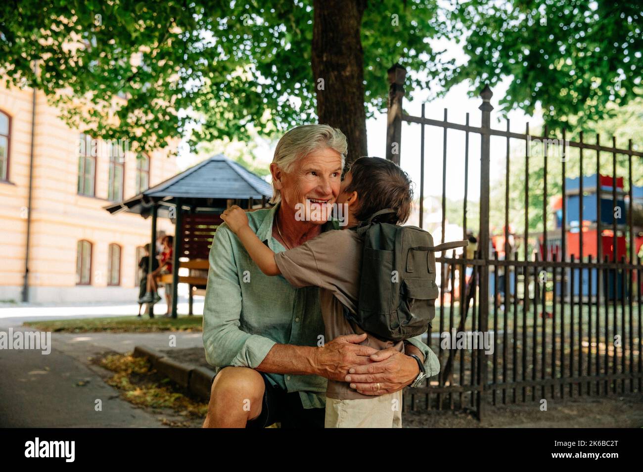 Un uomo sorridente che abbraccia il nipote fuori dal cancello della scuola Foto Stock