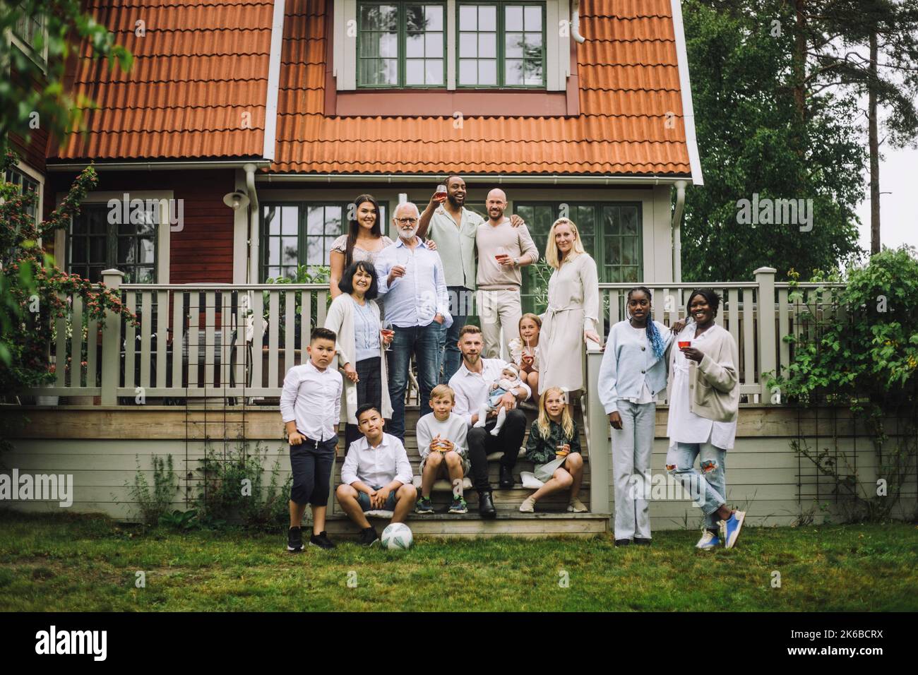 Famiglia multi-generazione con wineglass in posa al portico di fronte alla casa Foto Stock