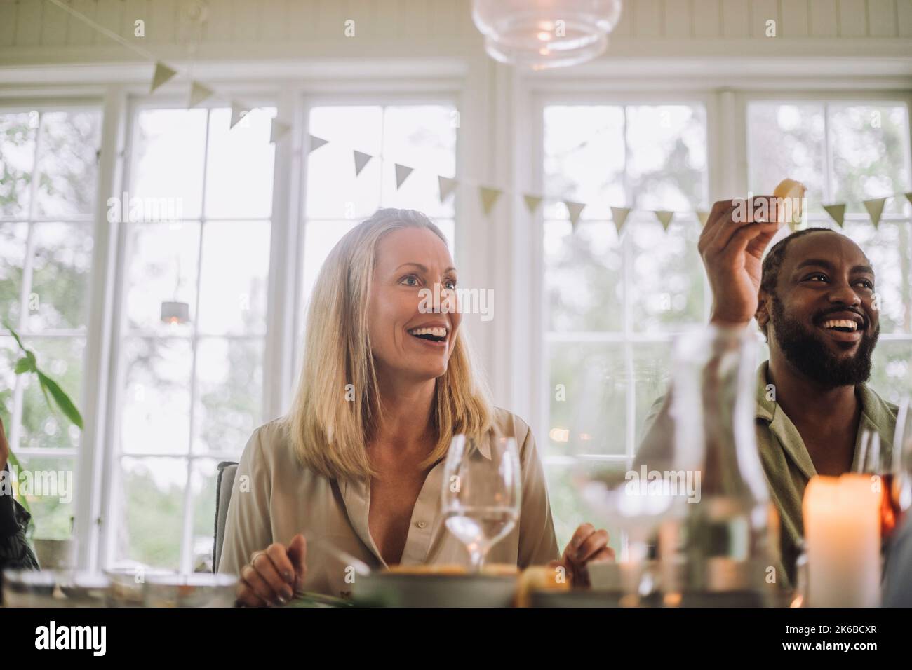 Donna sorpresa seduta da un amico maschio al tavolo da pranzo durante la festa Foto Stock