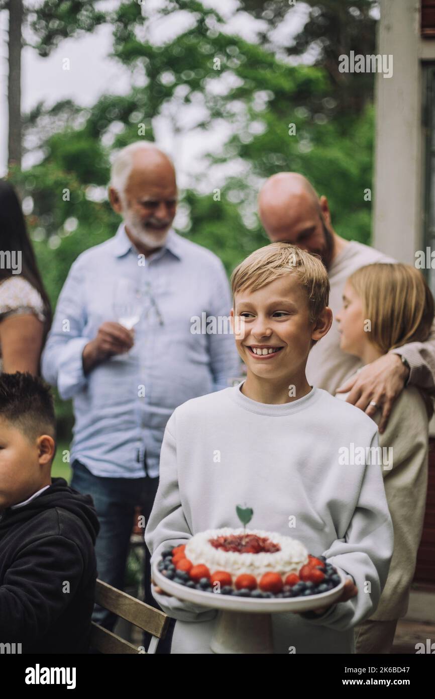 Ragazzo sorridente che tiene la torta alla festa di compleanno Foto Stock