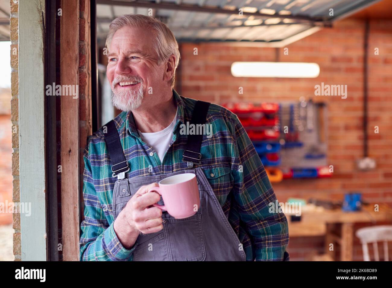 Ritratto di Senior Male indossare tute in officina Garage con bevanda calda Foto Stock
