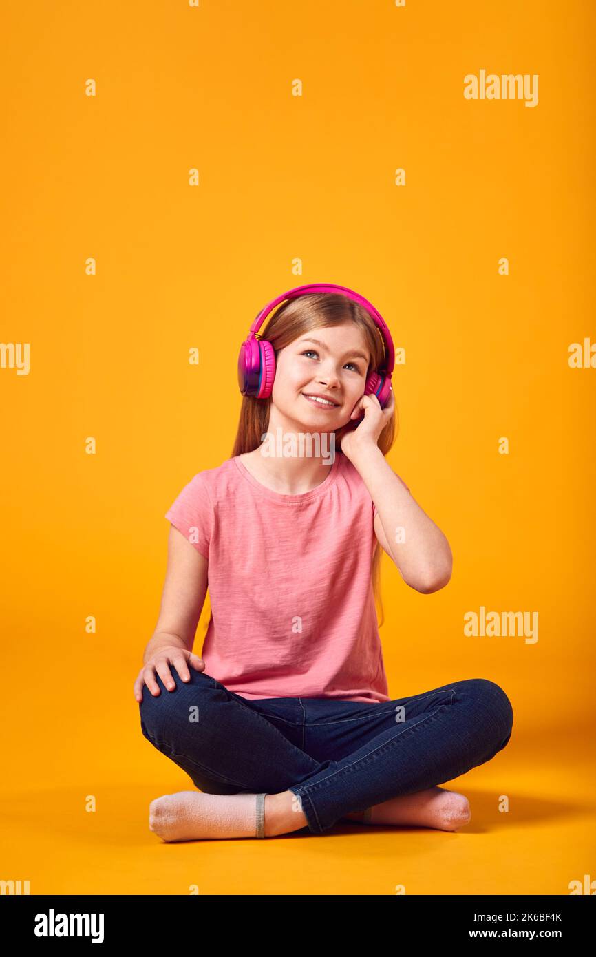 Studio Shot of Girl Listening to Music on Headphones with Hearts Graphic contro sfondo giallo Foto Stock