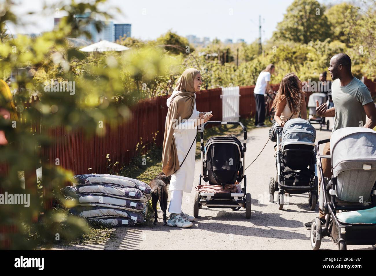 Vista laterale di una donna felice in hijab parlando con un amico da passeggino bambino sul sentiero Foto Stock