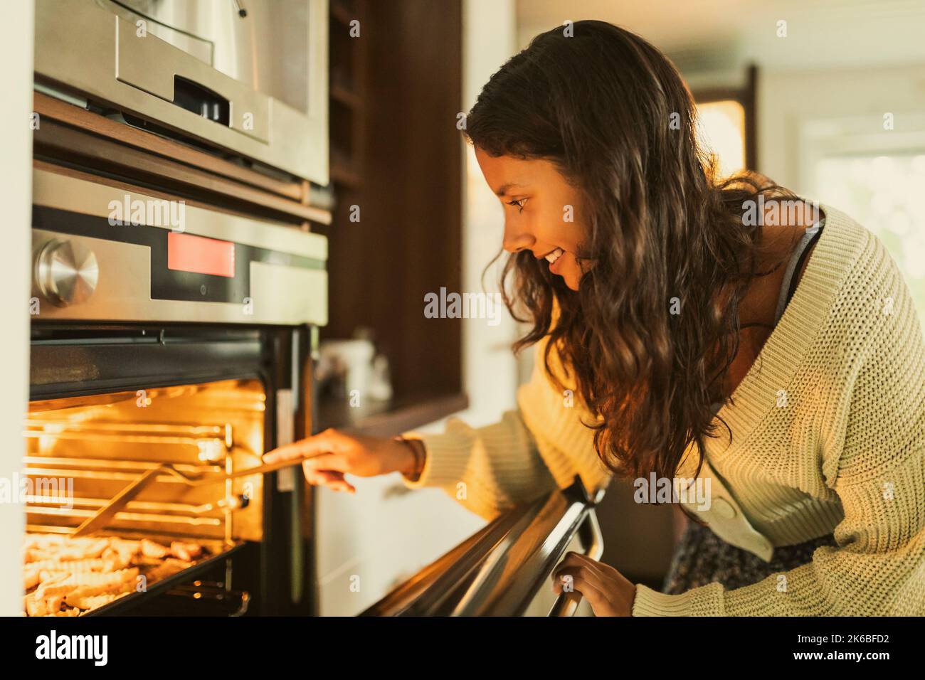Ragazza sorridente che controlla il cibo mentre apre la porta del forno Foto Stock